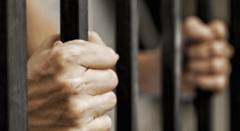 A jailed person's hands clenching the jail bars in a tight focused shot | Daniel Stark Law